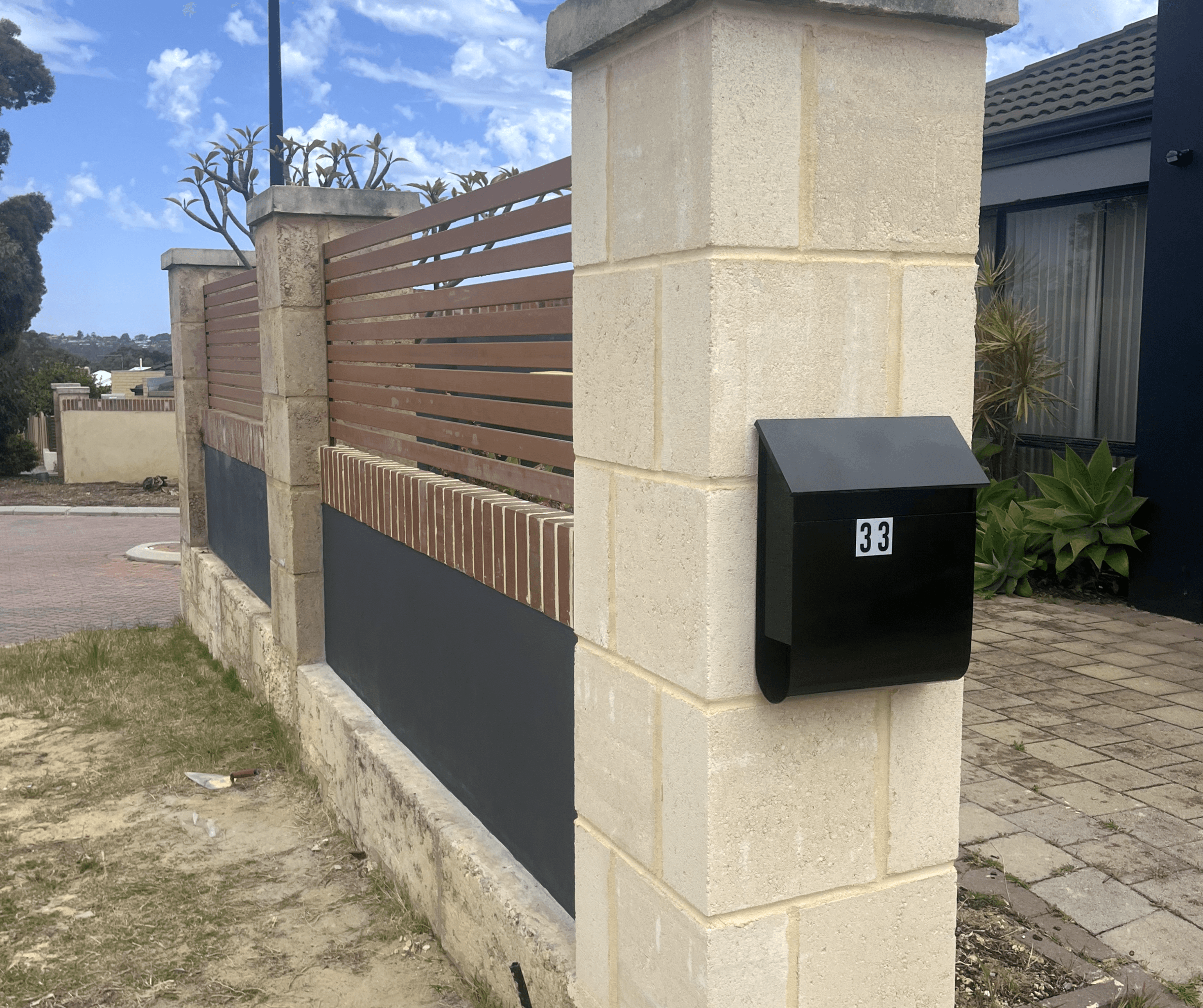 Limestone block pillar with a black letterbox beside a low red brick wall and timber slat infill
