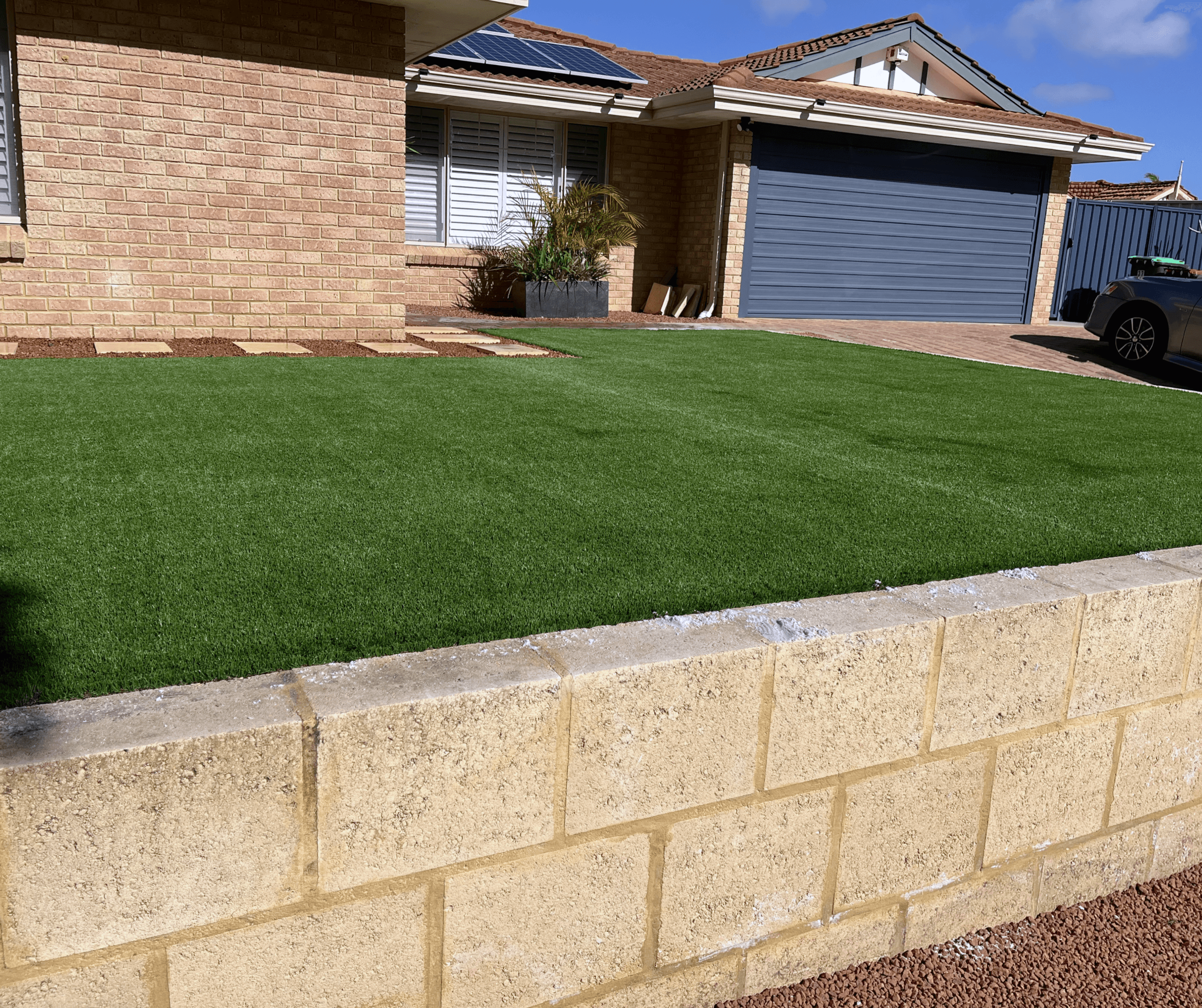 Front lawn above a new limestone block retaining wall, with the house and a tiled roof behind