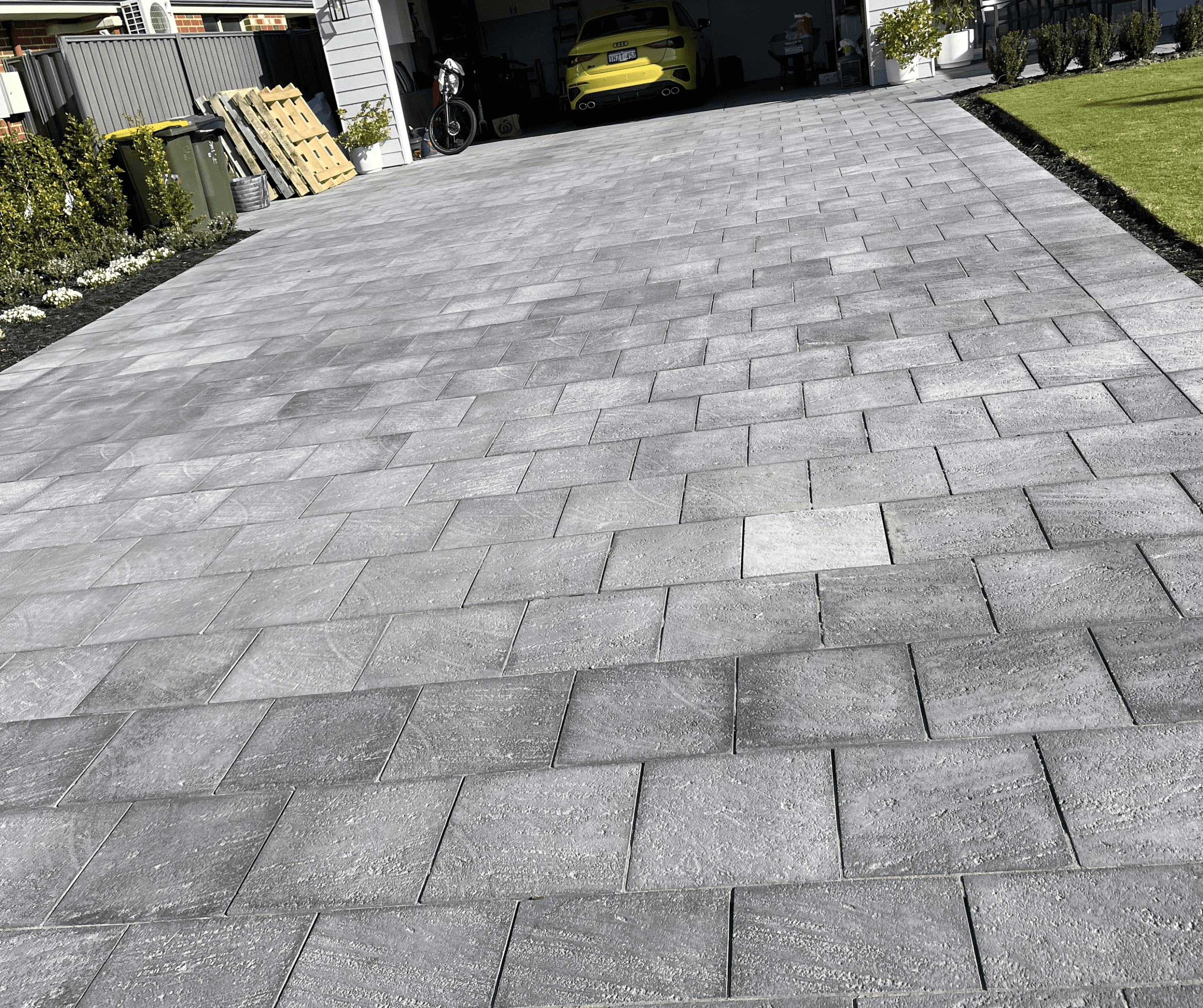 Charcoal paved driveway in a stretcher bond, with a car in the garage beyond