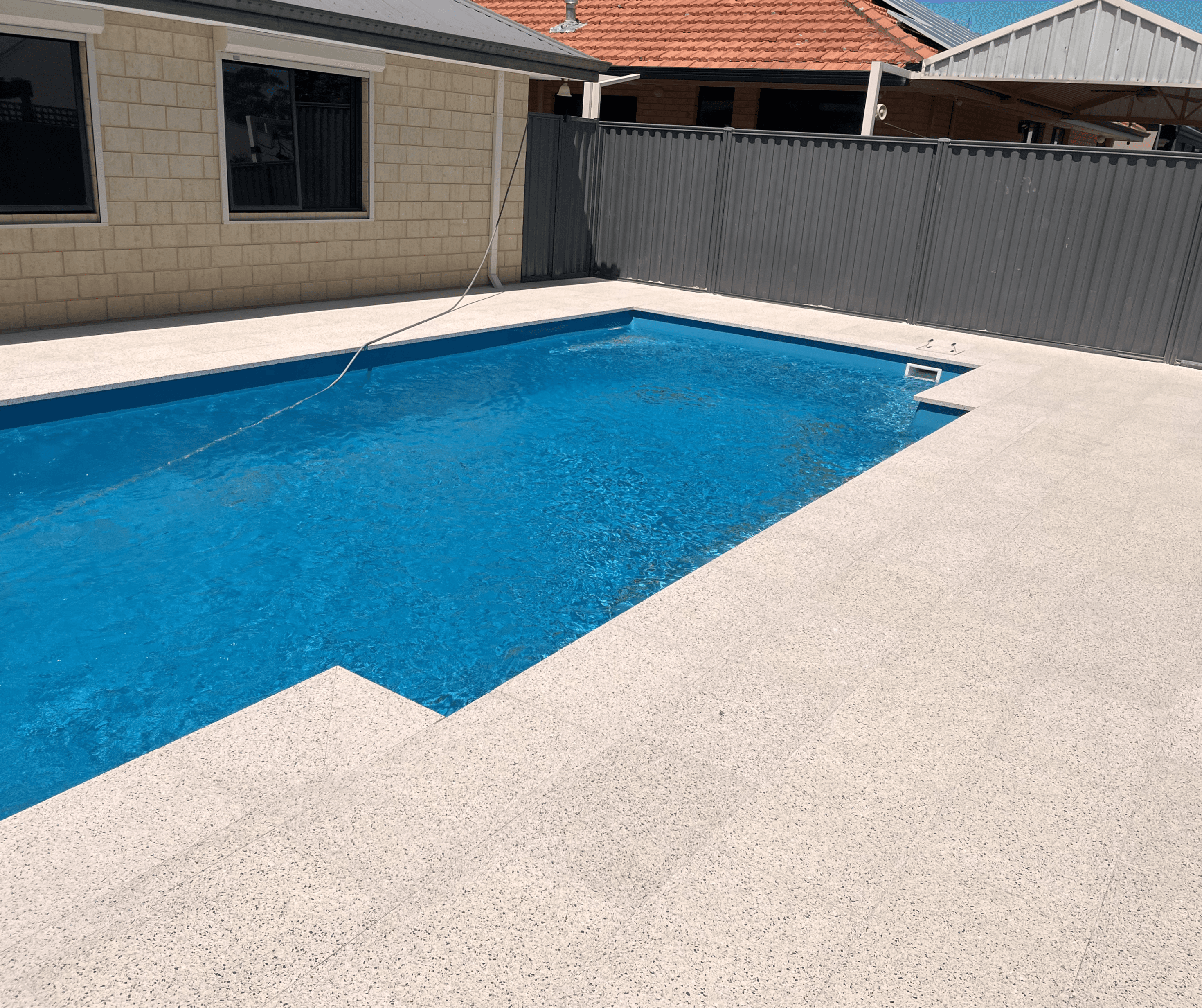 Pool surround in pale exposed aggregate beside a blue pool