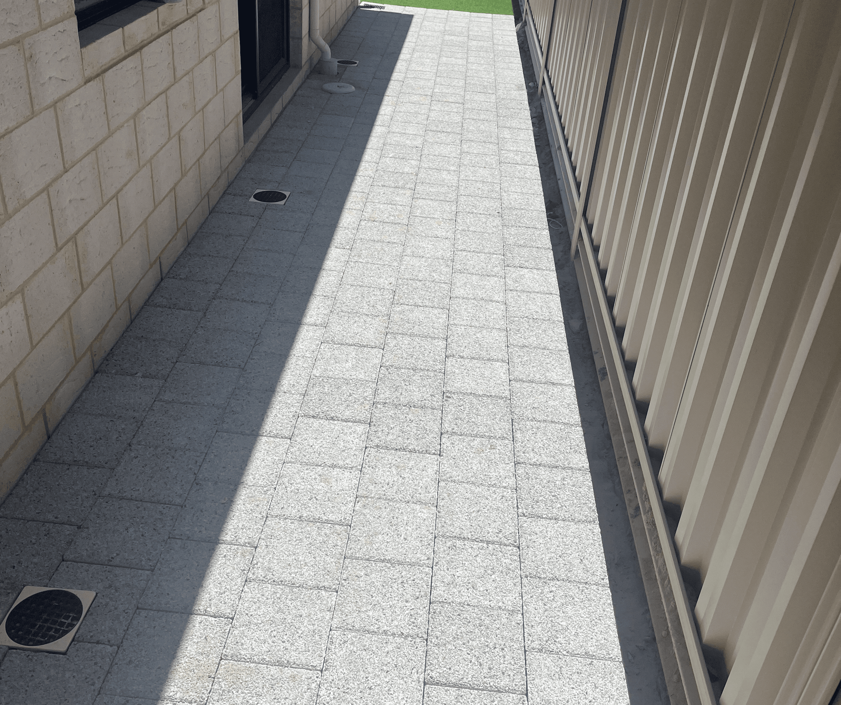 Light grey paved side path running between a house and a fence