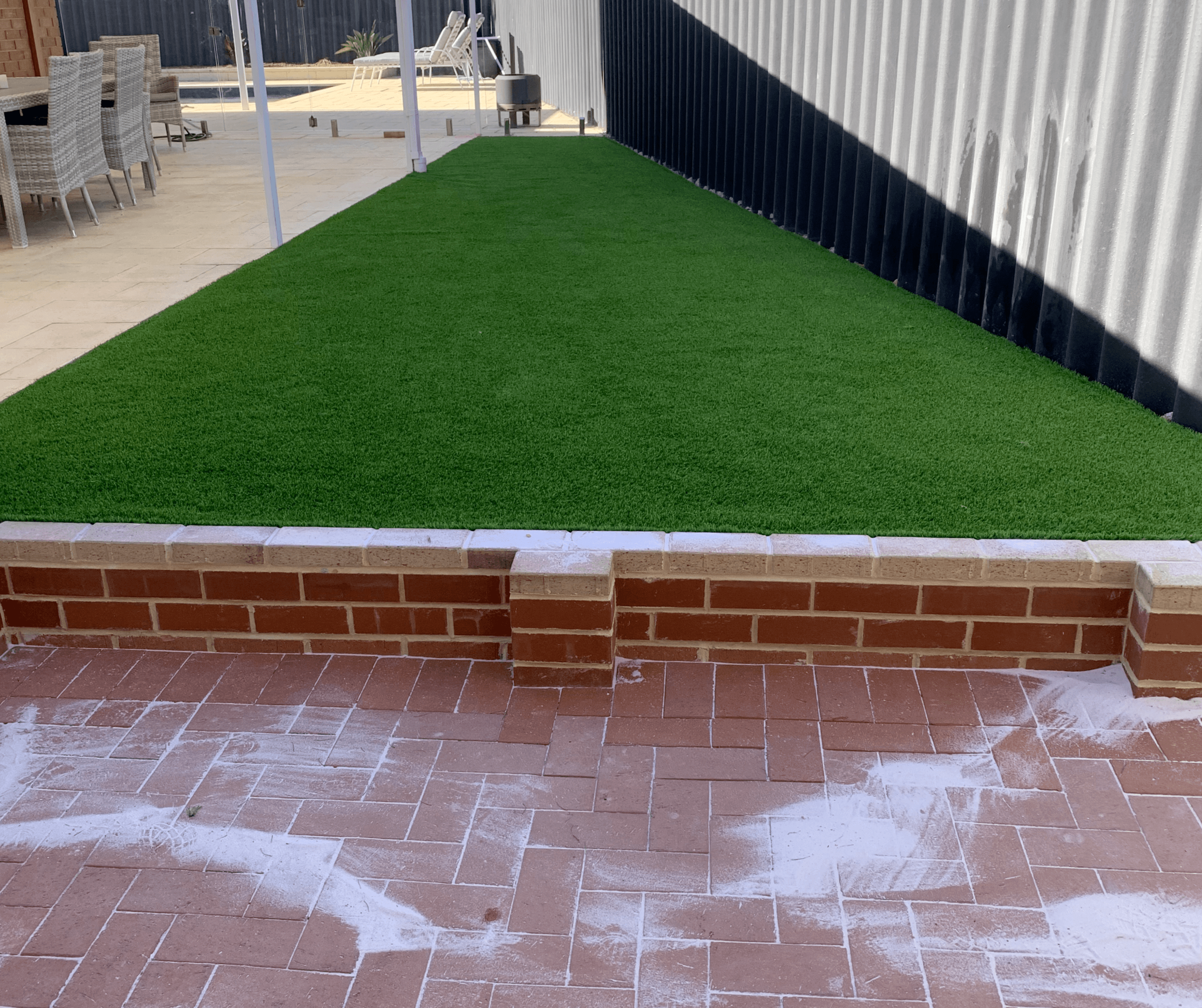 Artificial grass above a red brick edge beside a newly laid brick patio