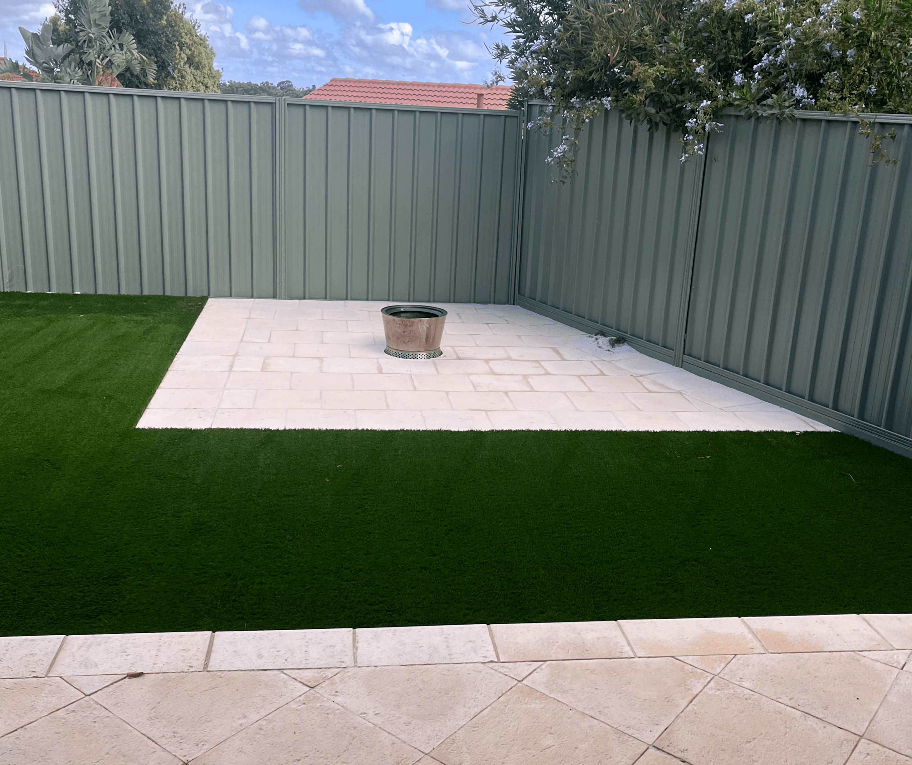 Artificial lawn around a pale paved courtyard with a fire pit