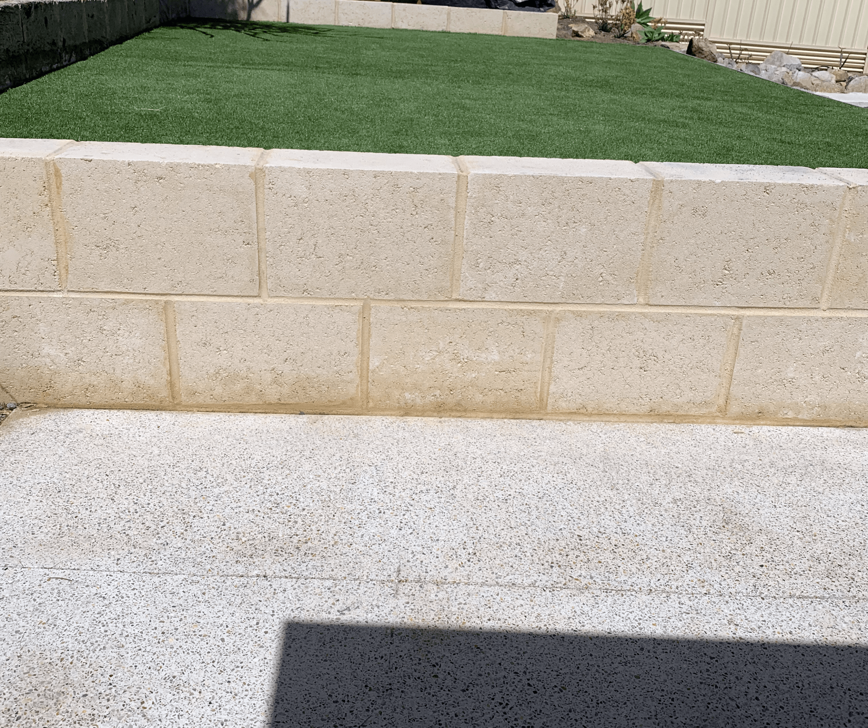 Limestone block retaining wall holding a raised artificial lawn above an exposed aggregate path
