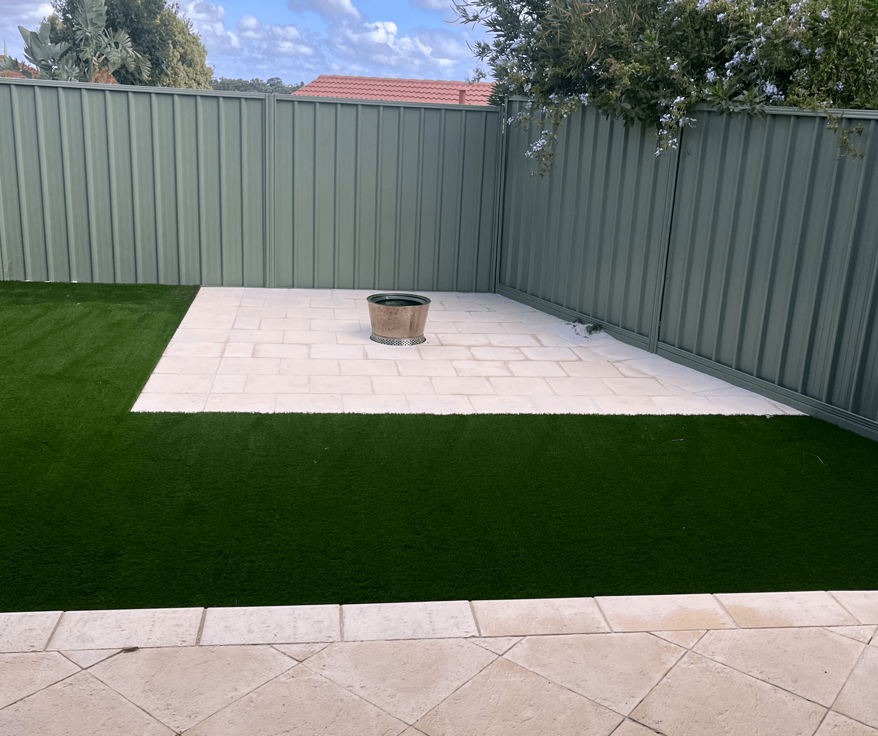 Artificial lawn around a pale paved courtyard with a fire pit