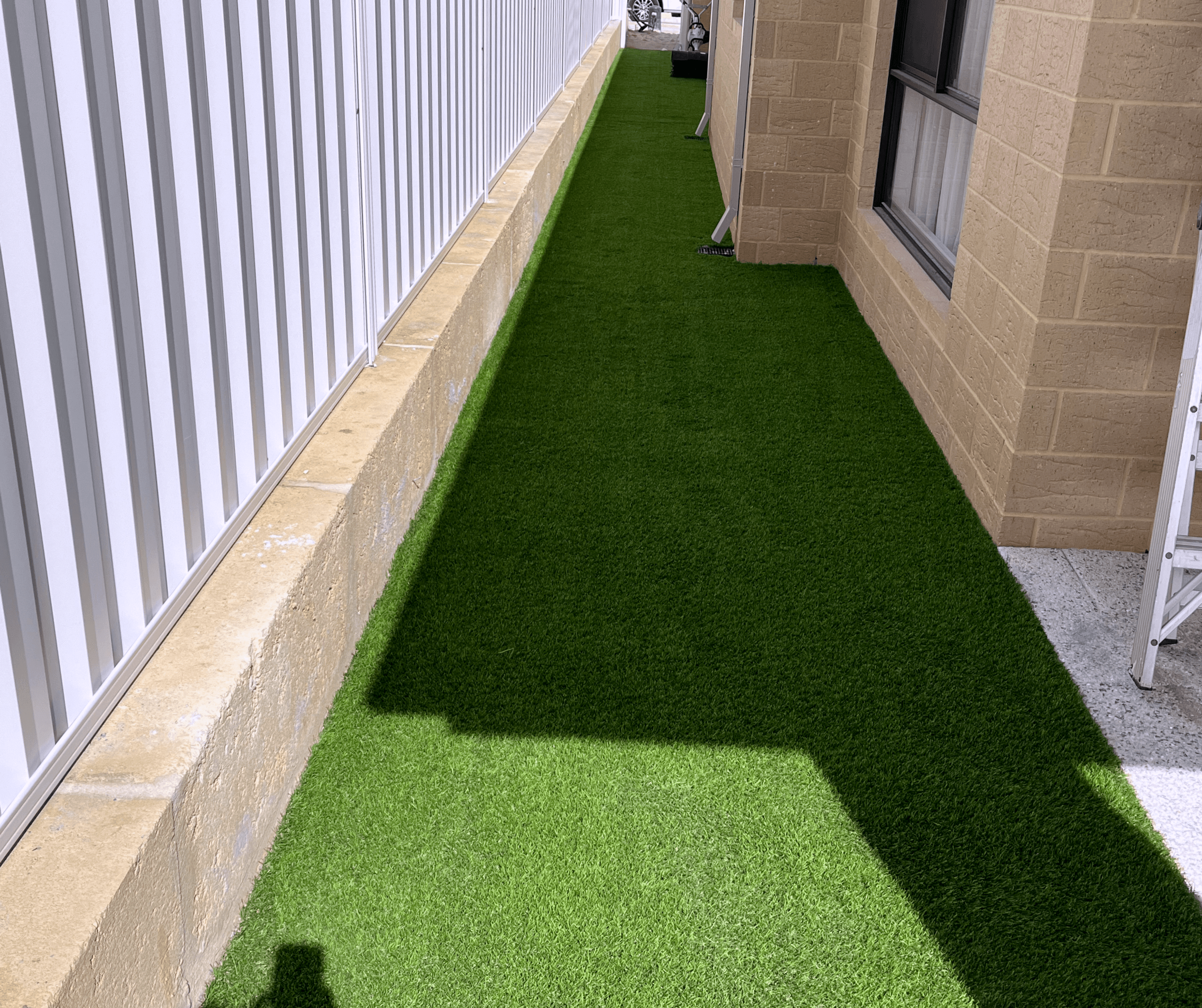 Artificial grass laid along a narrow side passage between a house and a fence