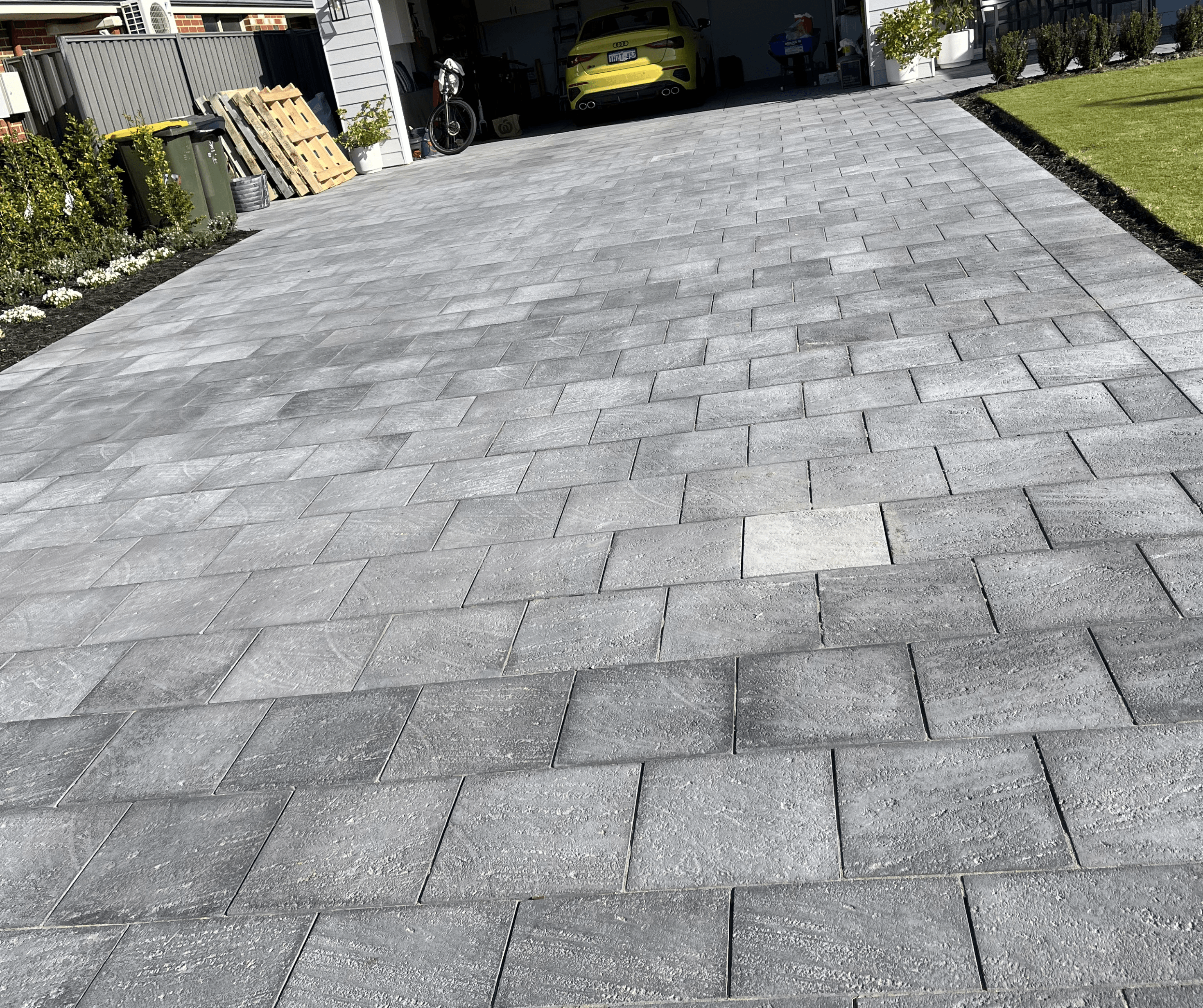Charcoal paved driveway in a stretcher bond, with a car in the garage beyond