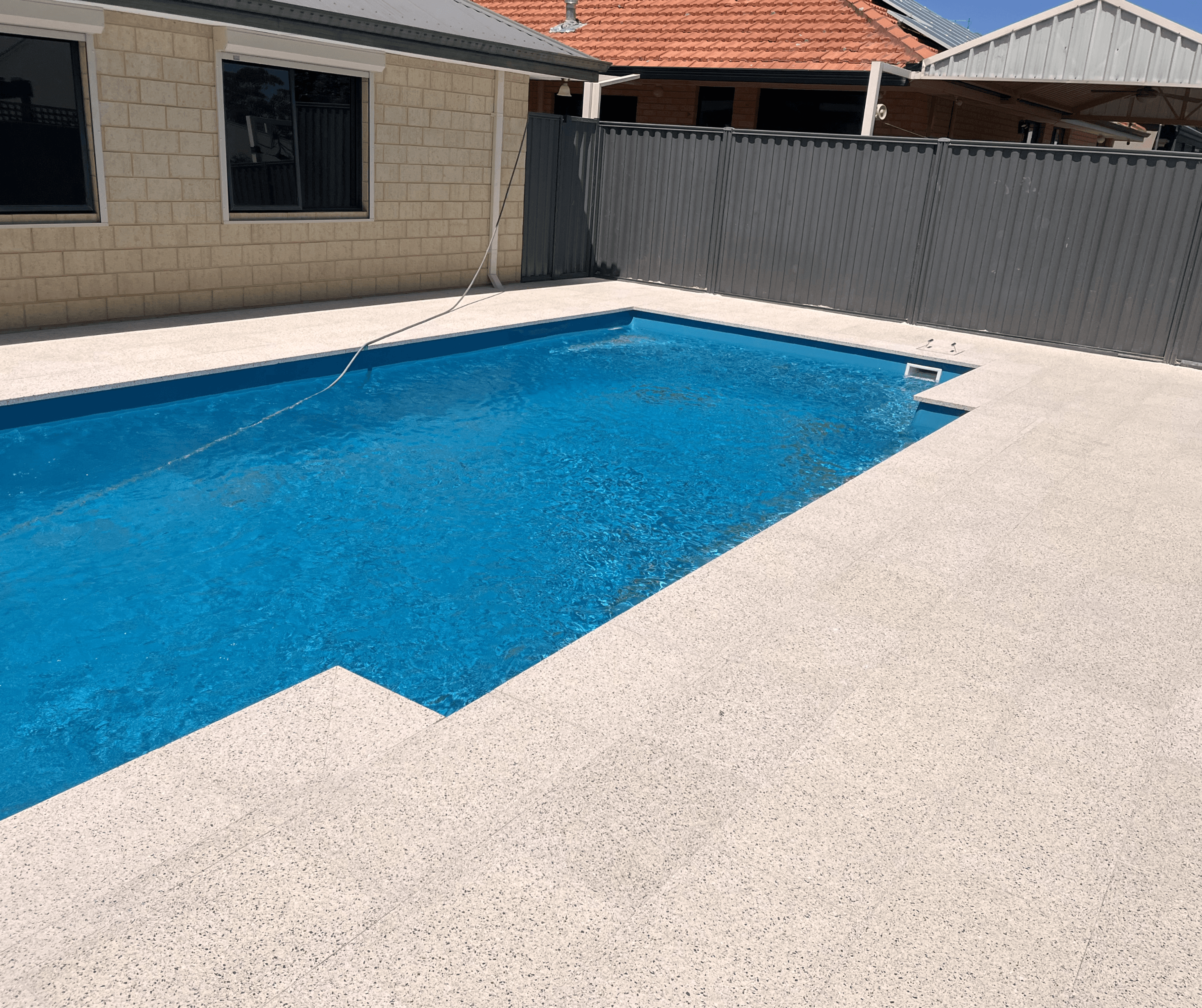 Pool surround in pale exposed aggregate beside a blue pool
